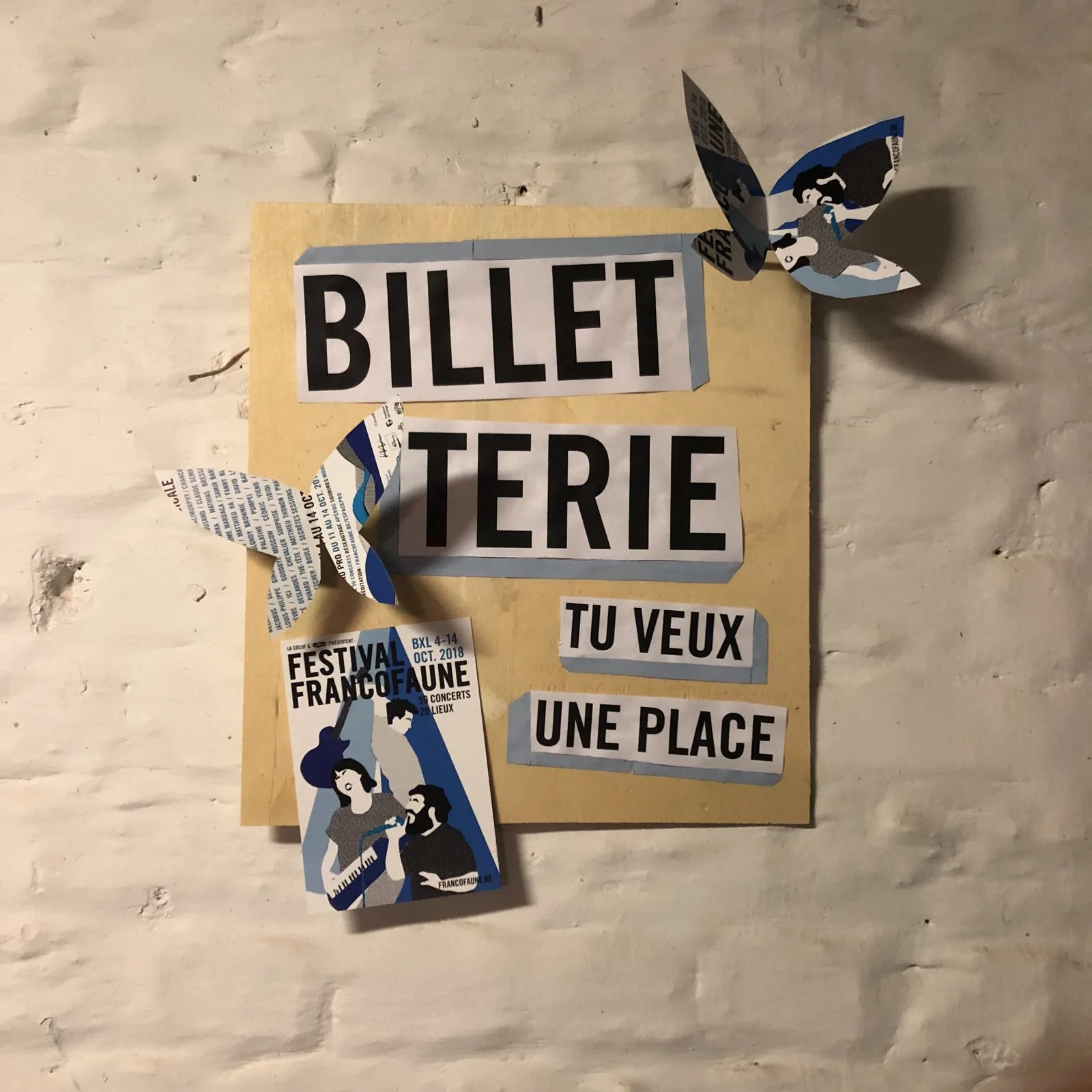 Panneau de carton beige fixé au mur : le mot BILLETTERIE en grands caractères noirs découpés sur bandes blanches, avec « tu veux une place », un flyer du festival et des formes découpées, assemblés au ruban adhésif à pois.