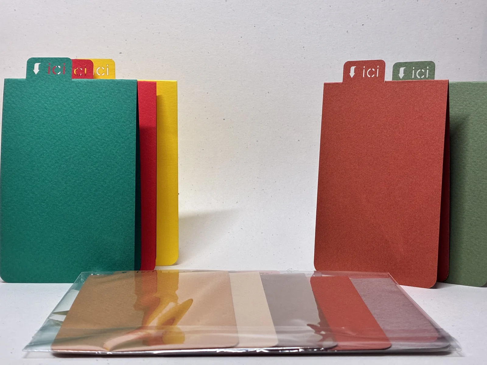 Cinq marque-pages debout côte à côte — vert, jaune, rouge — chacun portant le mot « ici » sous une flèche