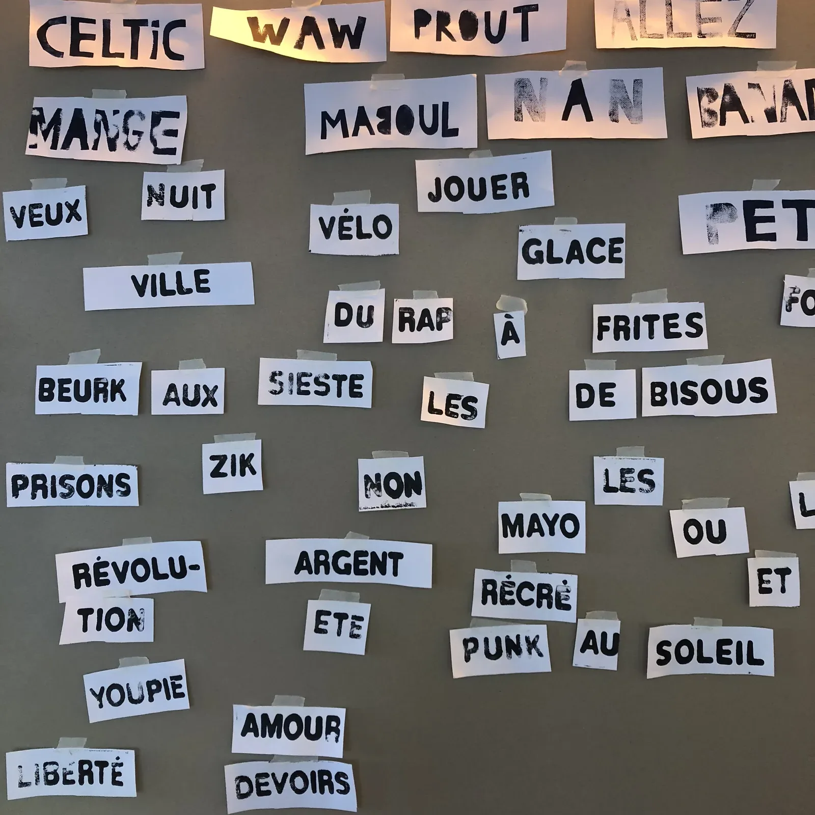 Des dizaines de tuiles de mots imprimées puis découpées, étalées sur une table : CELTIC, RÉVOLUTION, BEURK, VOLUPTÉ, PRISONS, SIESTE, FRITES
