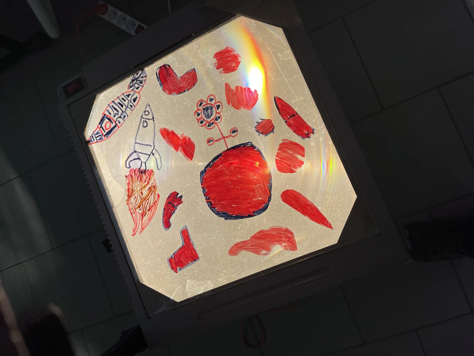 Une projection en couleur au plafond : formes rouges, dessins d’enfants, un cercle central